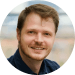 Smiling man with short hair in a blue shirt, set against a blurred background, representing innovation in technology and compliance.